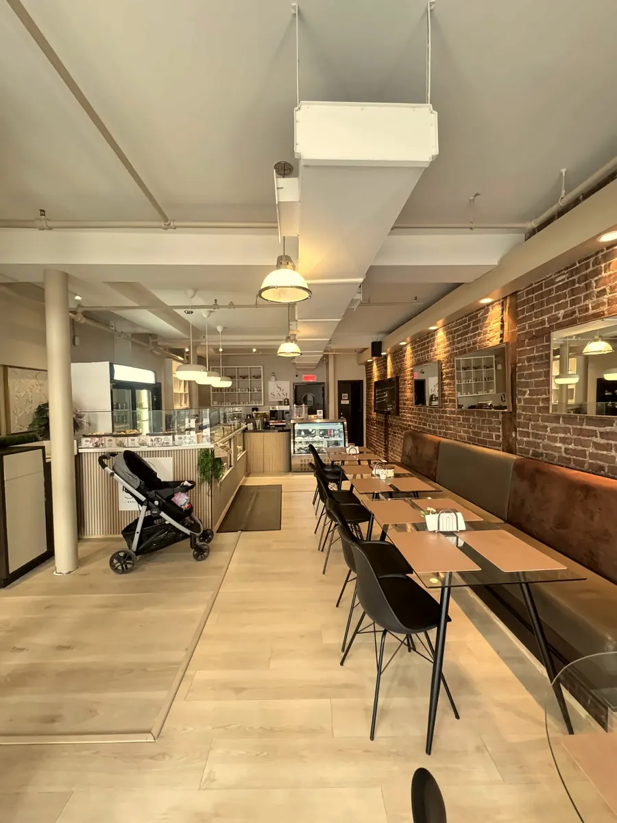 La salle : banquettes en cuir le long du mur de brique, tables et suspensions, comptoir au fond